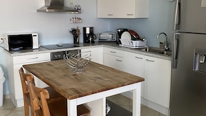Une cuisine de taille réduite avec des meubles blancs, une table en bois et un réfrigérateur en acier inoxydable.