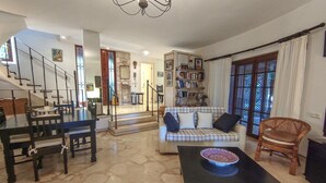 A spacious living room with a marble floor, a sofa set, a dining table, and a staircase leading to another level. - Villa for rent in Club Patara holiday village (Kaş)