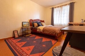 A bedroom with a bed, a nightstand, a desk, and a window with curtains.