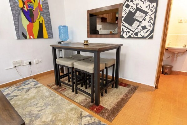 A small dining area with a table and four chairs, a blue water dispenser, and two artworks on the walls.