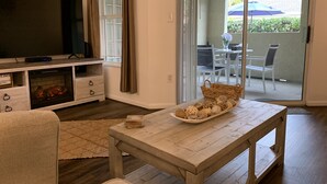 A living room with a TV, wooden entertainment unit, and a table with decorative items. - Literally: 15 steps to the Heated Pool/Ground Floor Condo/King Bed/Free Parking (Clearwater)