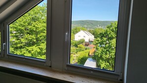 Een kamer met twee grote ramen met uitzicht op een groen landschap en een wit gebouw.