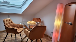 Een moderne kamer met dakraam, twee bruine leren fauteuils, een glazen tafel met een zacht voorwerp, en een hoge, cilindrische lamp.