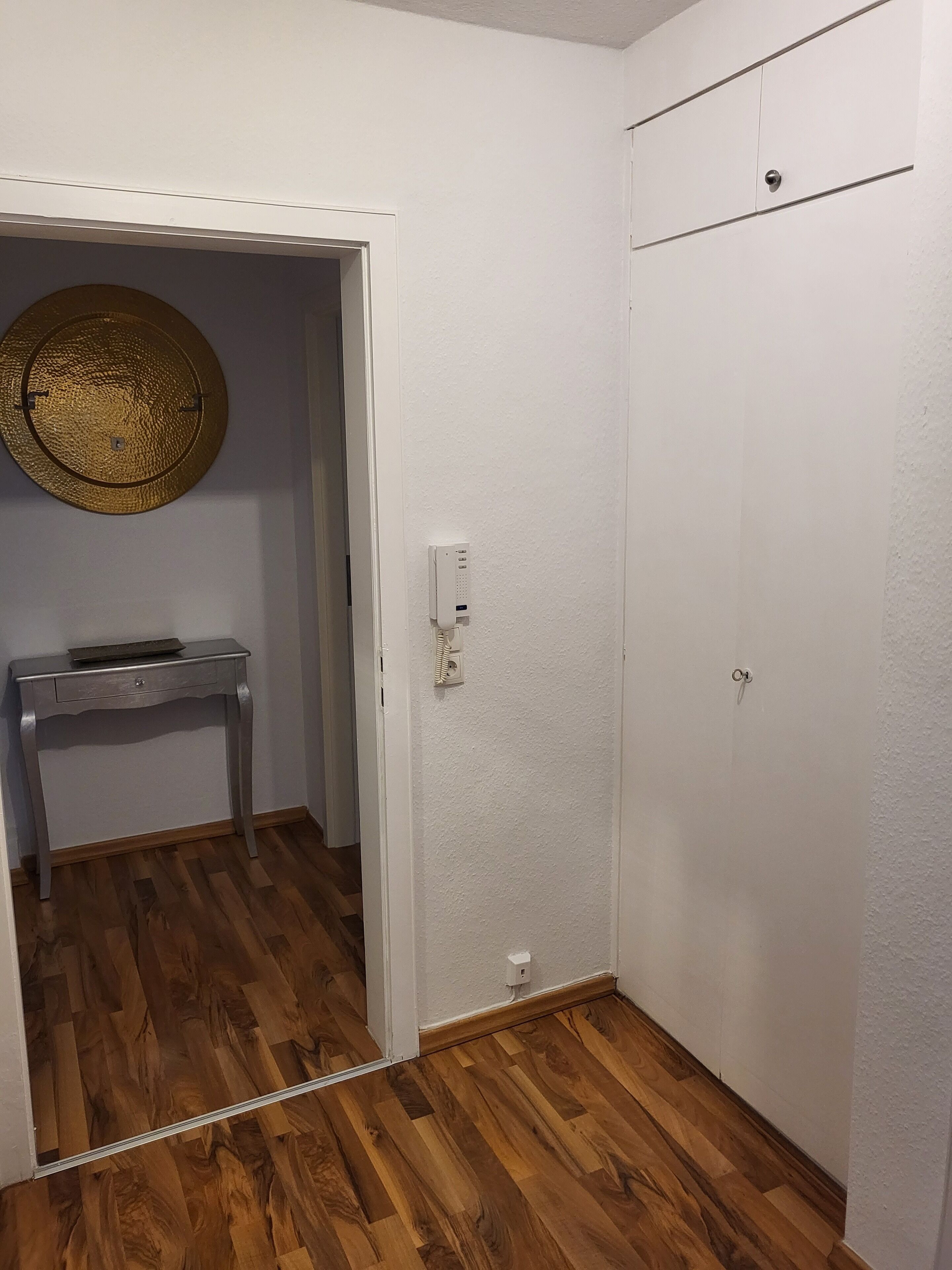 A room with a wooden floor, a white wardrobe, and a small table with a decorative item on it.