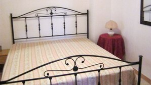 A single bed with a metal frame and a striped bedspread in a room with white walls and a small table with a lamp. - Holidays and relaxation 5 minutes from San Vito Lo Capo (custonaci)