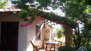 A stone-floored patio with a table and chairs, a wooden swing, and a pergola with flowering vines. - Holidays and relaxation 5 minutes from San Vito Lo Capo (custonaci)