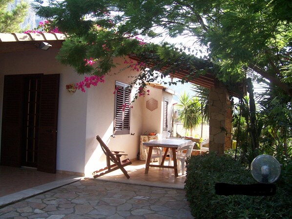 A stone-floored patio with a table and chairs, a wooden swing, and a pergola with flowering vines.