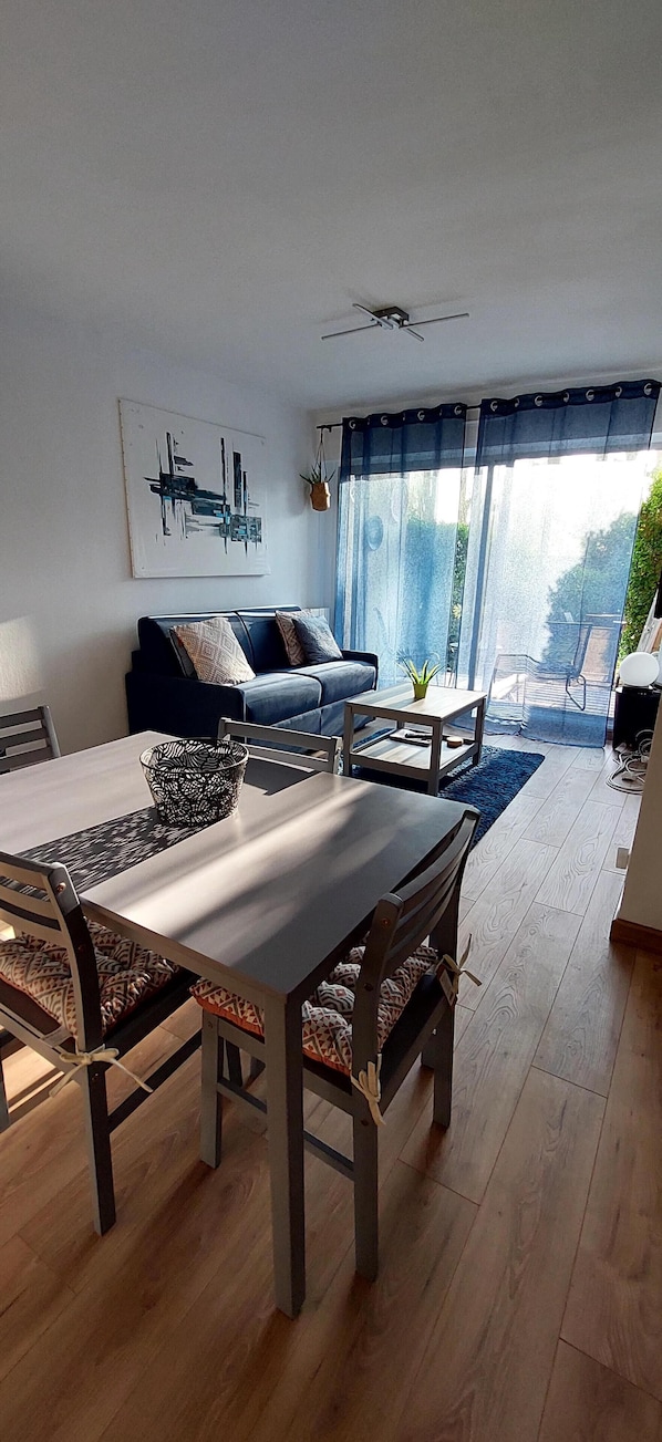 A modern living room with a dining table, sofa, and a view of the outdoors.