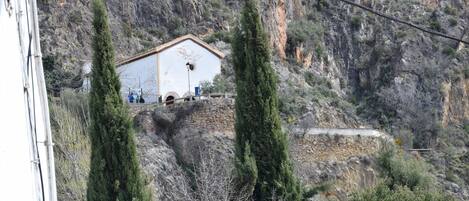 A building with a simple, white facade and a flat roof, situated on a rocky hillside with sparse vegetation.