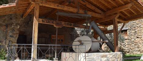 Un bâtiment rustique en pierre, doté d’un toit en bois et sur lequel est exposé un grand objet cylindrique.