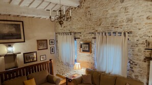 A cozy living room with two sofas, a coffee table with books, a chandelier, and a stone wall. - Amazing villa with swimming pool into the nature with view over the Adriatic sea (Marche)