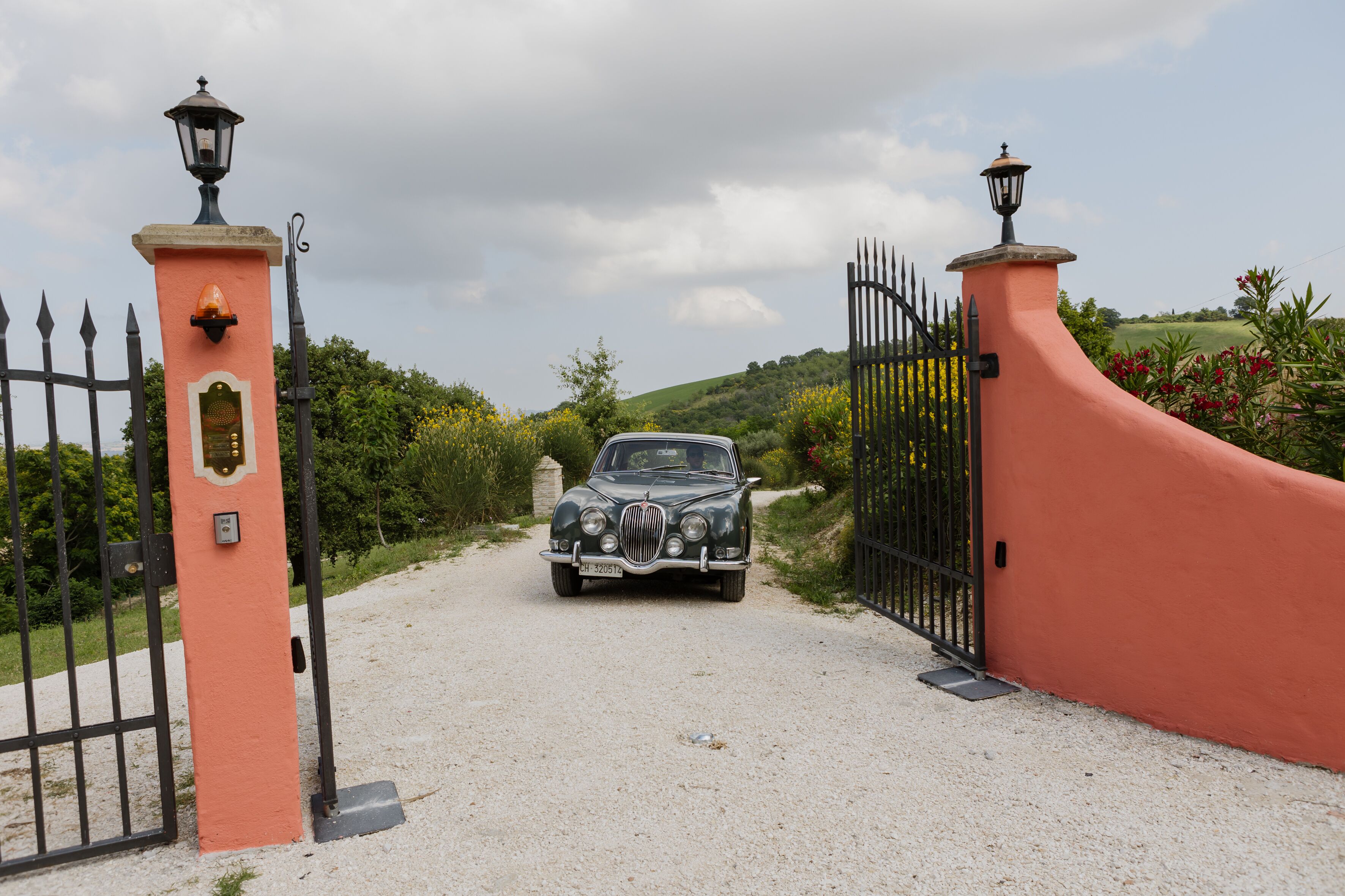 A vintage car approaching a gated entrance with a lamp post on each side.
