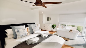 A modern bedroom with a large bed, a ceiling fan, a white bathtub, and a view of the outdoors. - Wrights Bay House★Sea View★Private Beach★Robe (Mount Benson)