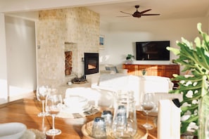 Een woonkamer met een open haard, een televisie en een eetgedeelte met een houten tafel gedekt voor een maaltijd.