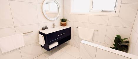 A modern bathroom with a dark vanity, a round mirror, a window, and a potted plant.