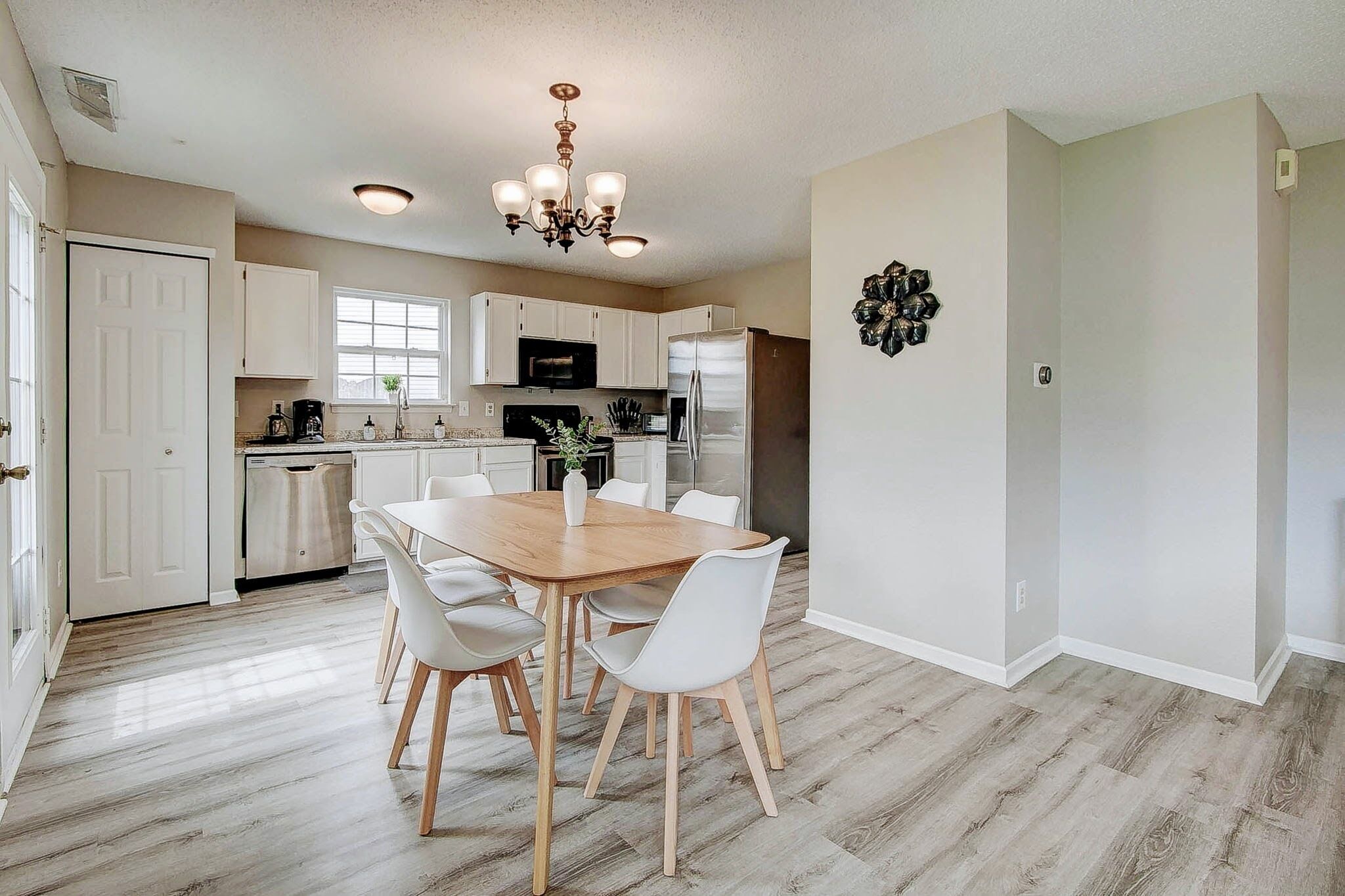 Une cuisine moderne avec des meubles blancs, une table à manger en bois et un lustre.