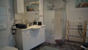 Casa de banho com sanita, lavatório, espelho, chuveiro e porta-toalhas.