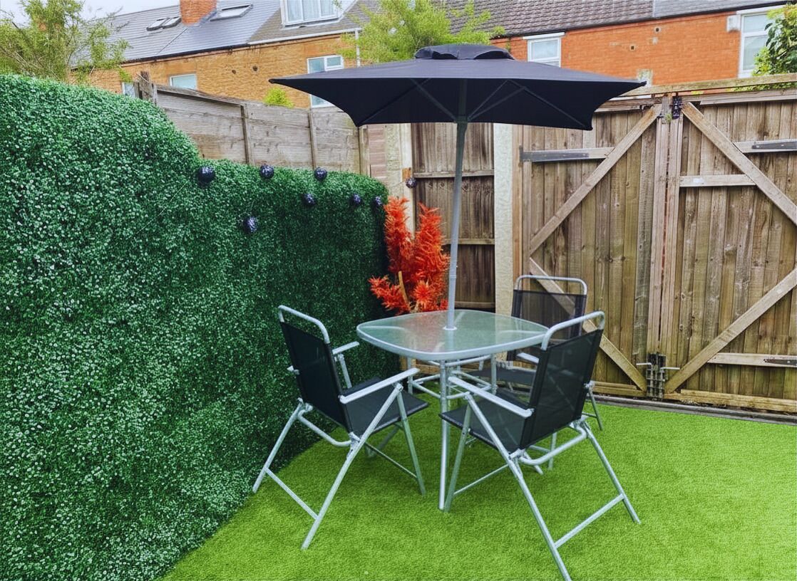 A patio with a round glass table and four chairs, a black umbrella, and a wooden fence in the background.