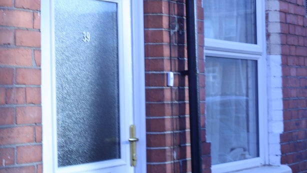 Une porte blanche avec un panneau de verre et le numéro « 39 » inscrit dessus, encastrée dans un mur de briques avec une fenêtre au-dessus.
