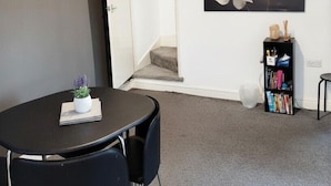 Une pièce moderne avec une table ronde, deux chaises, une bibliothèque, un grand tableau représentant des fleurs et un escalier menant à un autre niveau.