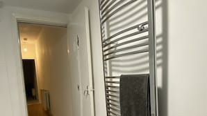 Une salle de bain équipée d’un porte-serviettes, d’une douche et d’une porte donnant sur une autre pièce.
