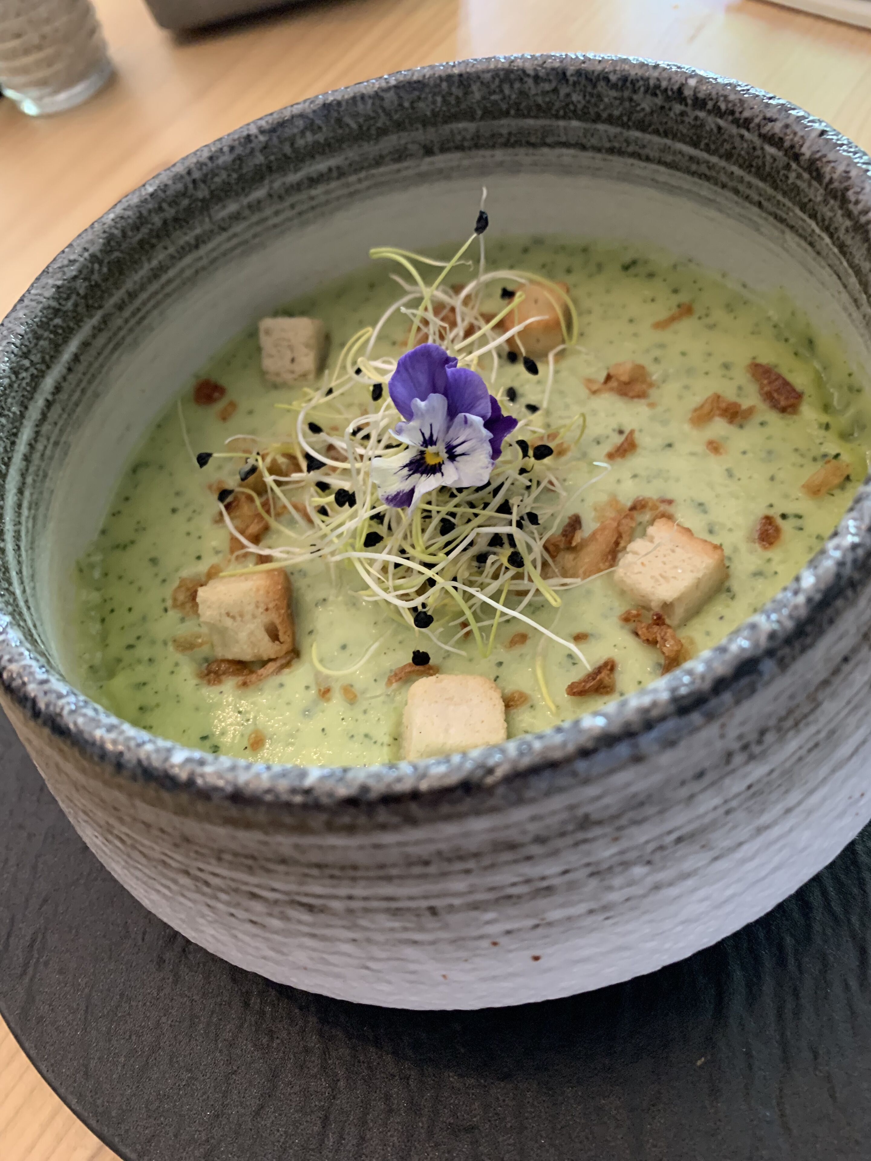 Een kom soep met een bloemversiering en croutons.