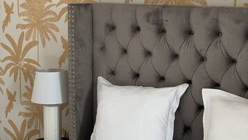 Un dormitorio con cabecera tapizada, ropa de cama blanca y una pared con estampado de hojas tropicales.