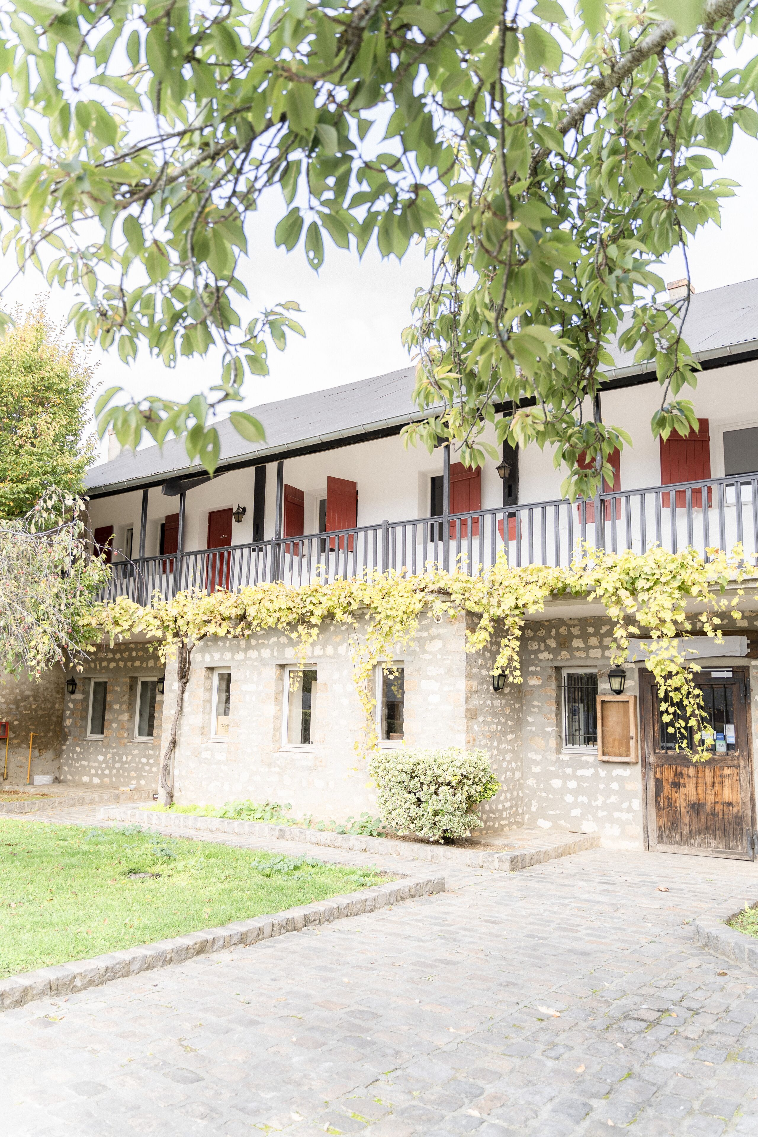 Un edificio de piedra con un balcón, una puerta de madera y un pequeño jardín.
