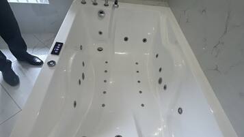 A large, rectangular, white bathtub with multiple jets, a control panel, and a window view.