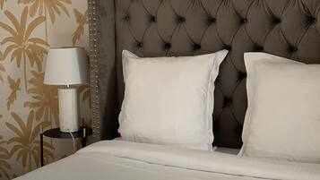 Una cama bien hecha con sábanas blancas y dos almohadas, un cabecero capitonado y una lámpara en una mesita de noche.
