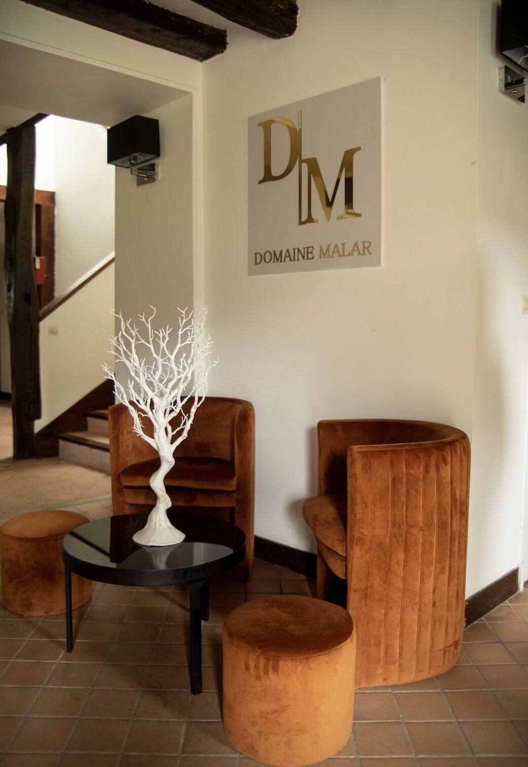 A modern interior with a staircase, a white tree sculpture on a table, and two brown upholstered chairs.