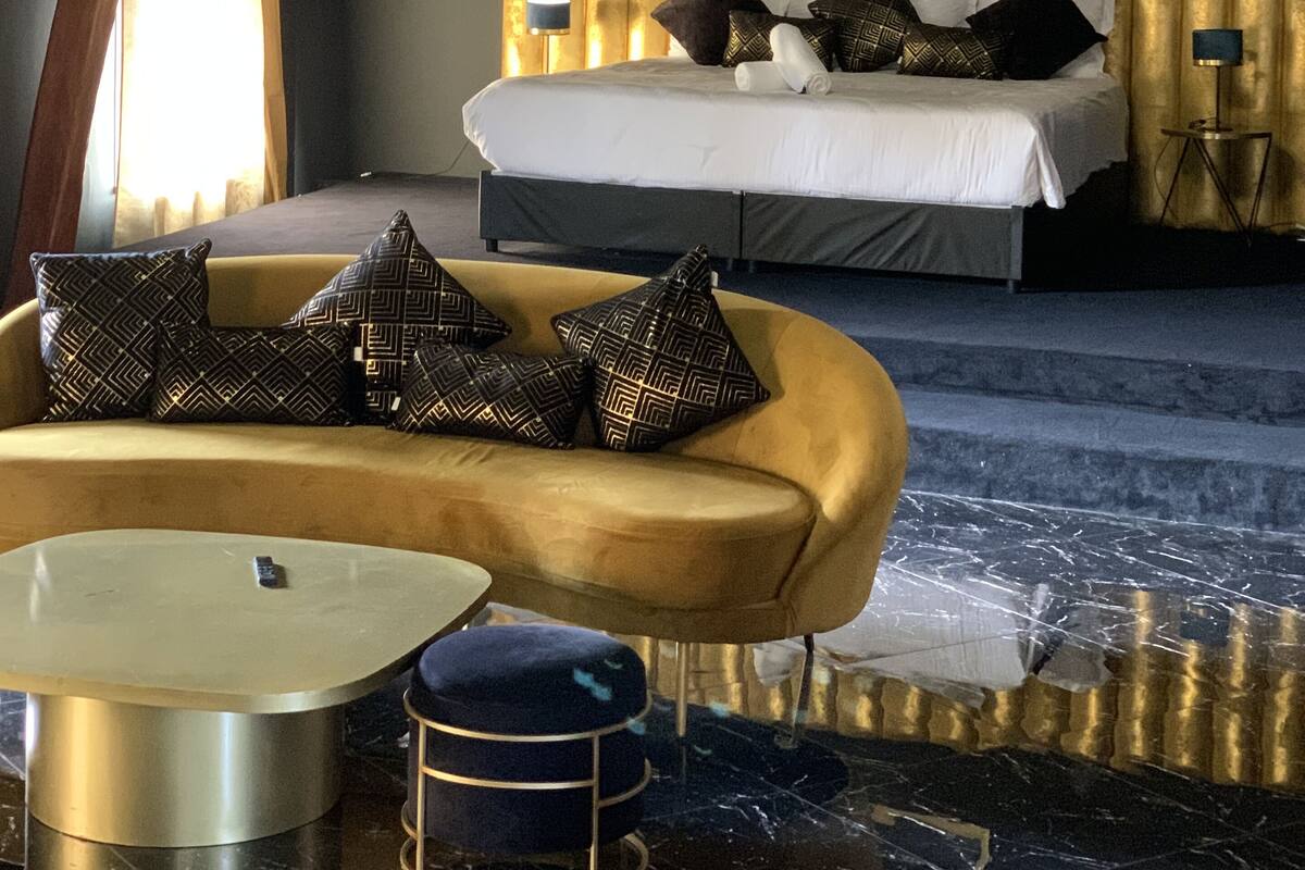 Un dormitorio con una cama grande, cabecera dorada, candelabro y sofá moderno.