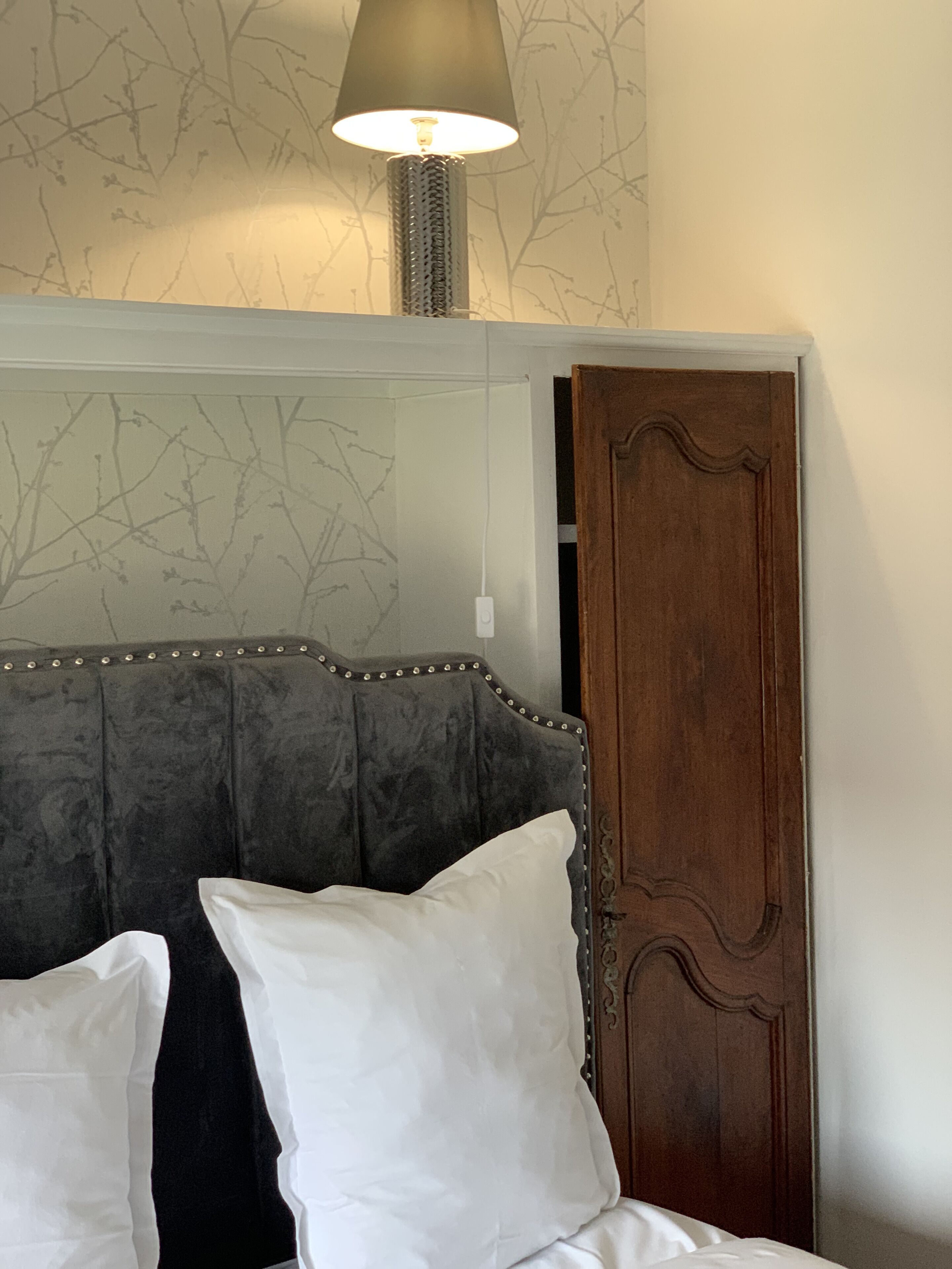 A bedroom with a tufted headboard, a wooden door, and a lamp.