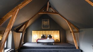 Un dormitorio con techo inclinado, una cama con almohadas, un cabecero y dos lámparas de noche.