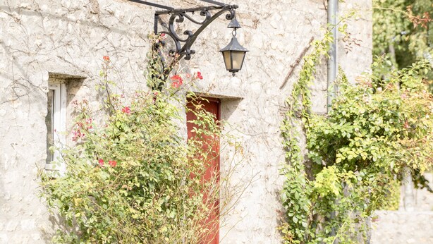 Un edificio de piedra con una puerta roja, una ventana pequeña y una lámpara fijada a la pared.