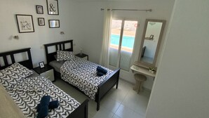 Een hotelkamer met twee bedden, een badkamer en uitzicht op een zwembad.