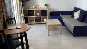 Een woonkamer met een blauwe bank, een houten salontafel, een eettafel met stoelen en een tv op een dressoir.
