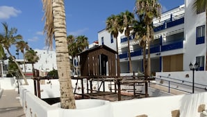 Een wit gebouw met blauwe балконы, palmbomen en een houten constructie op de voorgrond.