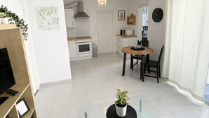 Een moderne woonkamer met een televisie, een eettafel en een keuken op de achtergrond.