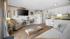 Ett kompakt bostadsutrymme med ett litet kök, en matplats och en sittgrupp med en soffa och en bänk.