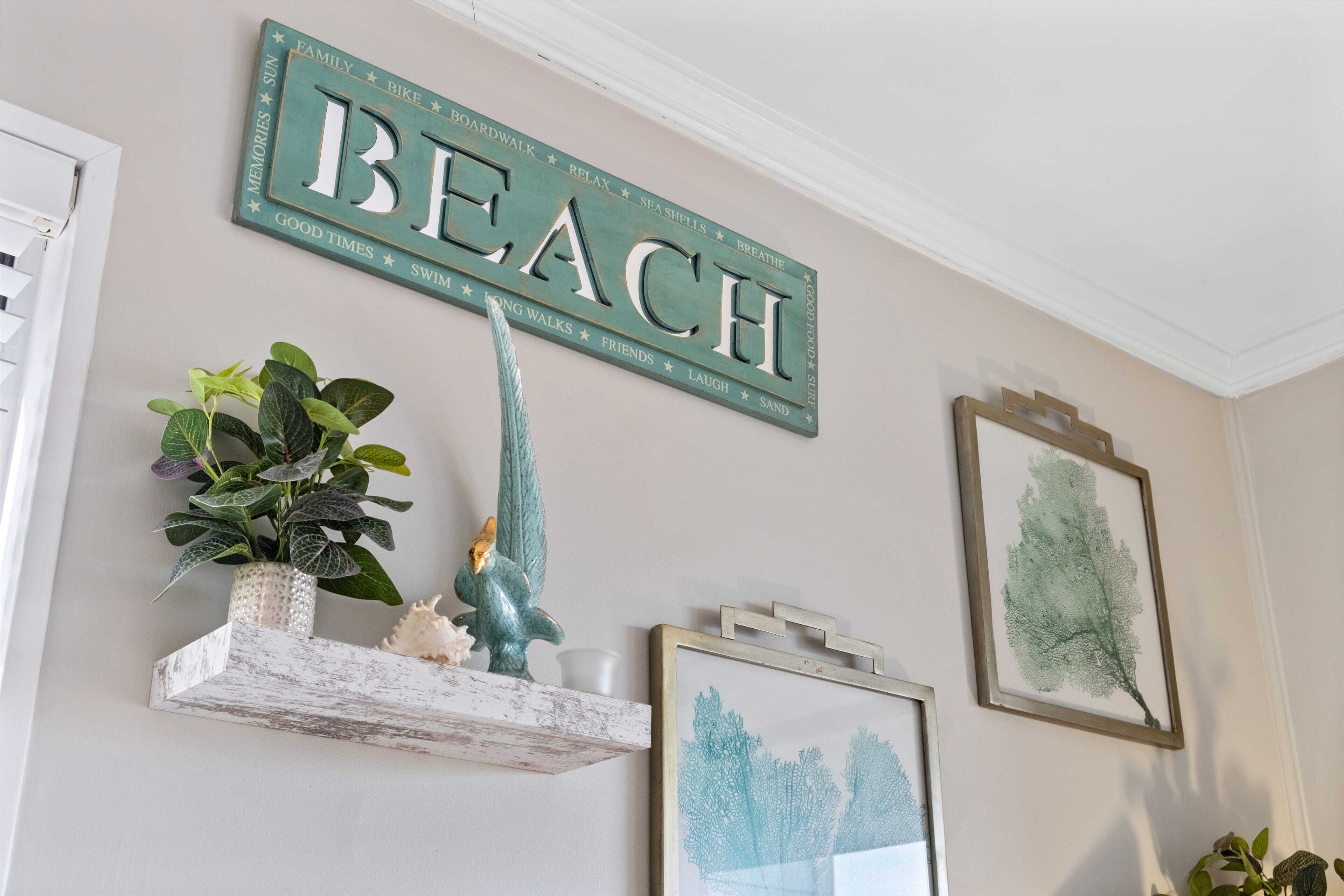 Eine Wand mit einem großen Schild, auf dem 'BEACH' steht, umgeben von Dekoration und gerahmten Kunstwerken.