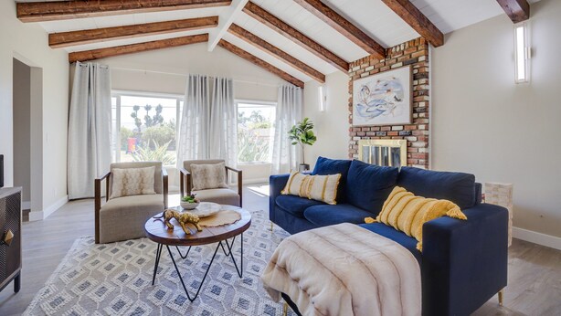 A living room with a blue sofa, beige armchairs, a round coffee table, and a fireplace with a brick wall.