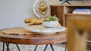 A round wooden table with a decorative bowl and a piece of food, a decorative wall piece, and a bookshelf with books.
