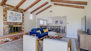 A spacious living room with a blue sofa, a fireplace, and a dining area in the background.