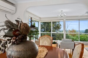 A dining area with a large window, a chandelier, and a decorative vase with dried plants.