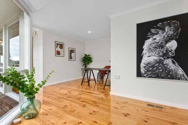 A modern interior with wooden flooring, a dining area with a table and chairs, and a large framed artwork on the wall.