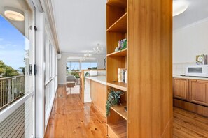 A spacious balcony with wooden flooring, a dining area with chairs and a table, and a kitchen with wooden cabinets and a microwave. - BerwickHills Stylish 3 BdrmHome *Free Wifi*NetFlix (Berwick)