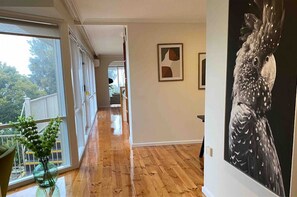 Un pasillo con suelo de madera, una puerta de cristal que da al exterior y un cuadro grande en blanco y negro en la pared.