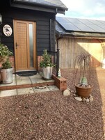 Uma casa com porta de madeira, placa de boas-vindas e plantas em vasos.