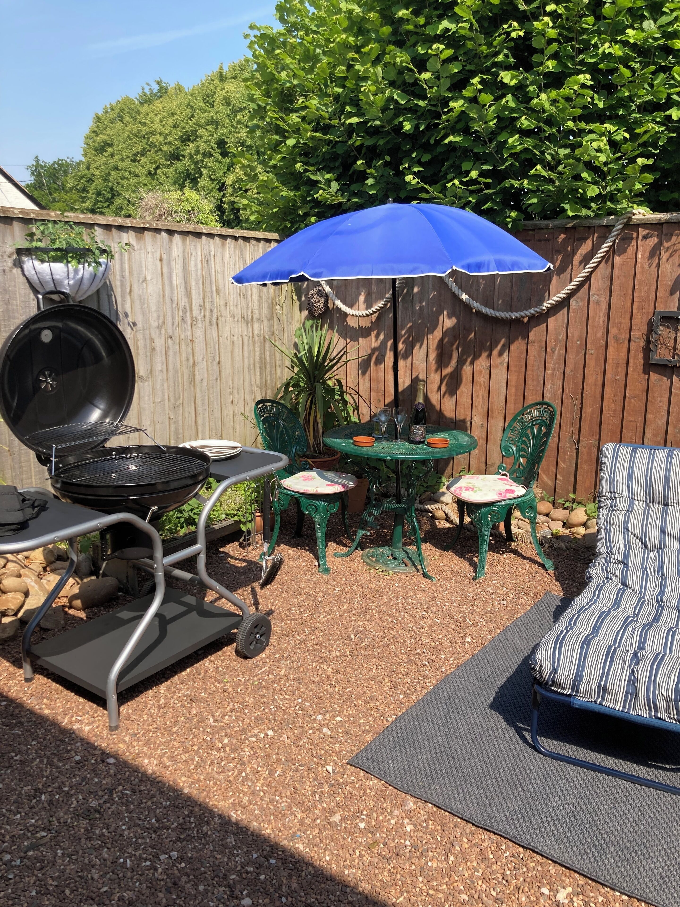 Un patio trasero con una parrilla, una mesa con sillas y una sombrilla azul.